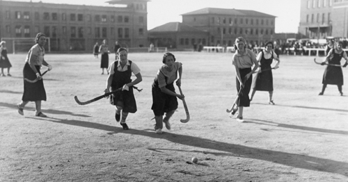 Partit d'hoquei entre l'equip femení de la Residencia i l'equip del Club de Campo, 1933. Al fons, els edificis de la Residencia.